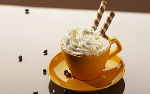 brown ceramic teacup and saucer filled with wafer stick and whip cream