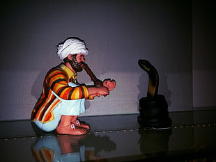 man sitting while using flute and cobra on black basket ceramic figurine, snake, Aladdin, museum, toys