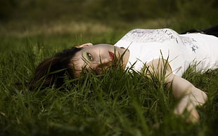 woman in white tank top lying down on grass field
