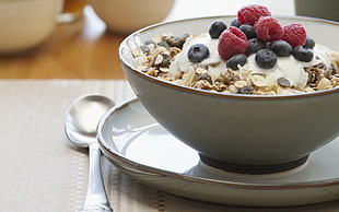 oatmeal with raspberry in white ceramic bowl on plate beside spoon