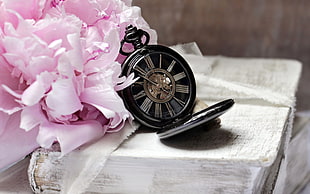 round black pocket watch and pink petaled flower on table