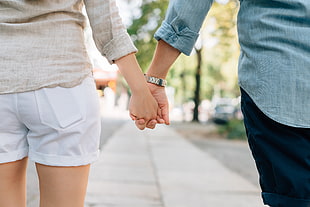 couple holding hands while walking on pavement