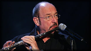 man wearing eyeglasses playing black flute in front of black microphone