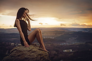 woman wearing black midi dress sitting on mountain cliff