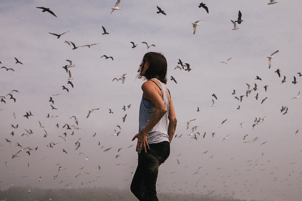 woman in gray tank top straight standing below flock of flying birds HD wallpaper