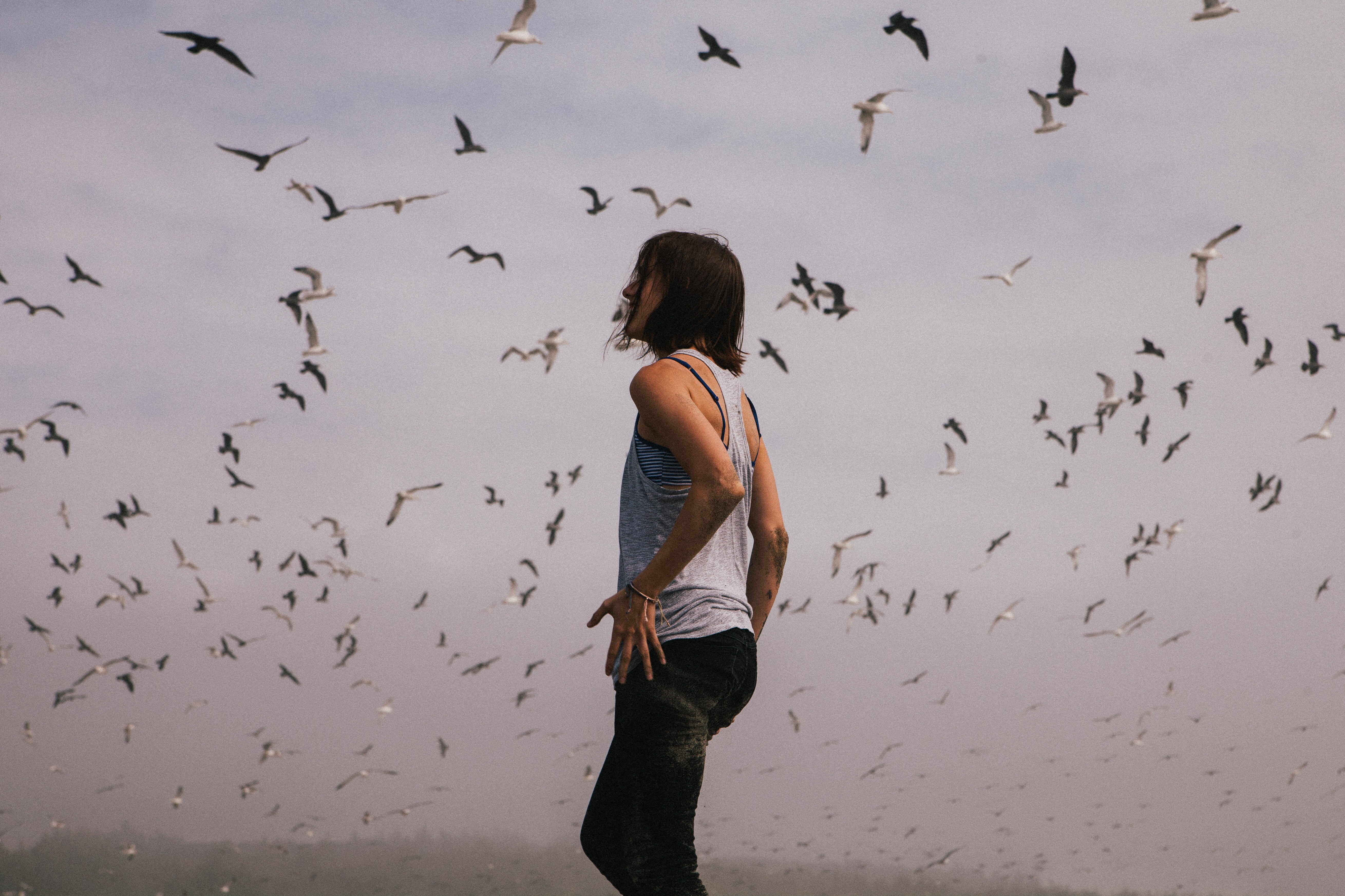 woman in gray tank top straight standing below flock of flying birds