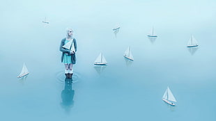 woman in teal midi dress with gray cardigan on body of water holding paper boat