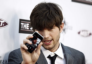 man in grey blazer holding turned on black smartphone