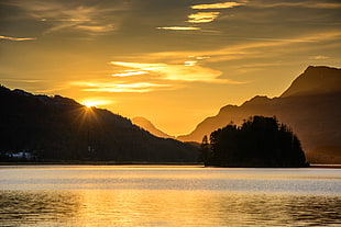 silhouette of island beside body of water under peeping sun HD wallpaper