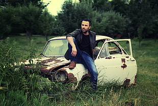 photography of man in black jacket sitting on rusted white car