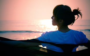 woman in white shirt facing ocean during sun set