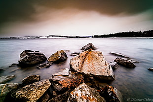 landscape photo of stones in body of water under cloudy sky during day time