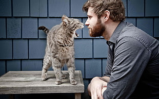 man in front of grey cat opening mouth