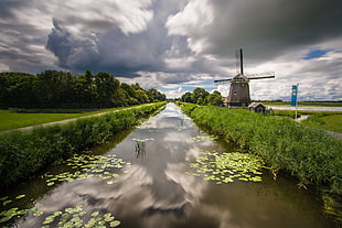 landscape photography of river between green grass near of windmill HD wallpaper