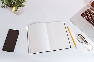 high angle photo of iPhone 6, notebook, pencil, eyeglasses, and MacBook Air