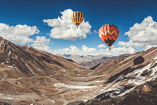yellow and orange hot air balloon near brown rocky mountain