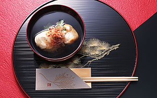closeup photo of cooked food on red ceramic bowl and red and black serving tray with chopsticks