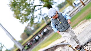toddler in gray vest and blue dress shirt walking on gray railroad