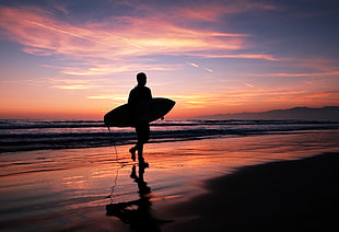 person holding surfboard while walking in the beach at night time, los angeles