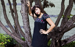 woman wearing black and purple square neckline cap-sleeved dress leaning on tree trunk