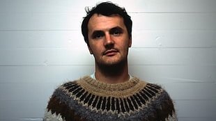 man wearing black and brown knitted shirt standing against white background