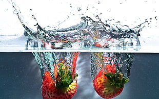 two red submerge strawberry fruits on water