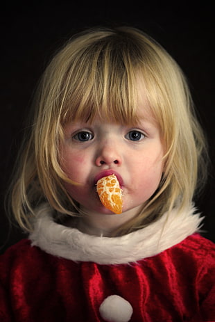 girl eating sliced orange fruit wearing red Santa dress