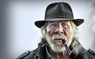 photography of man with black hat smoking tobacco with tobacco pipe