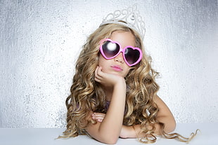 woman with blonde hair wearing pink heart sunglasses and silver tiara taking photo