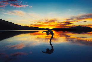 person leaning backward on body of water during golden hour