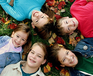 five children laying on green grass