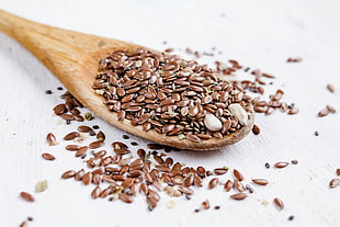 closeup photo of beans on beige wooden spatula, flax seeds