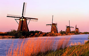 wooden windmills near body of water during sunset
