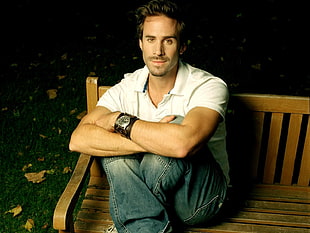 black haired man wearing white polo shirt sitting on brown bench