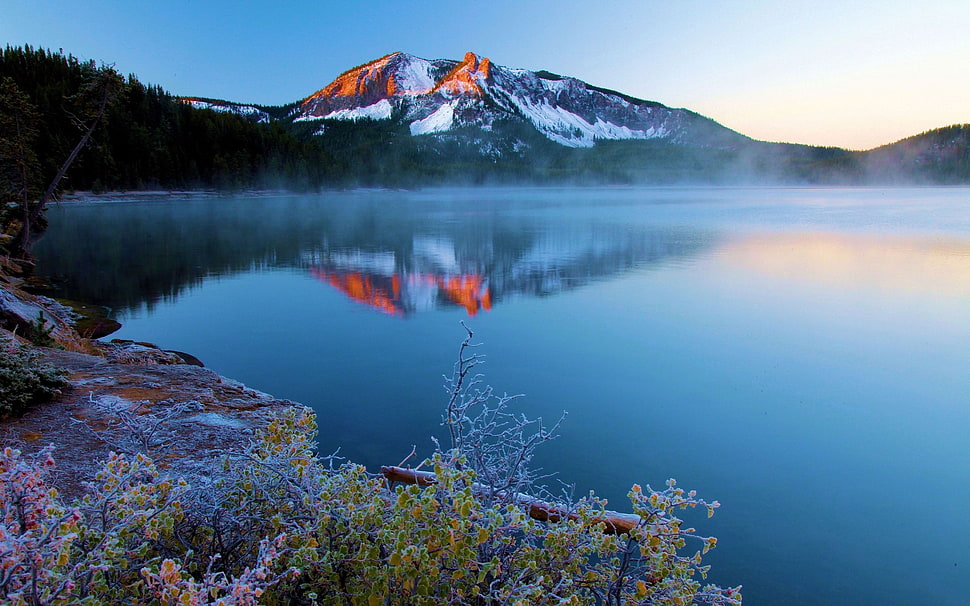 body of water near mountain under blue sky HD wallpaper