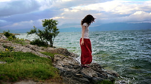 woman in white t-shirt and red pants near sea during daytime
