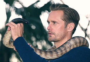 close-up photography of man in blue sweatshirt carrying brown snake