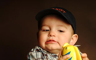 boy holding yellow plastic toy wearing black cap