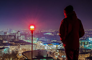 man wearing red jacket and hat standing in front of red LED tower light