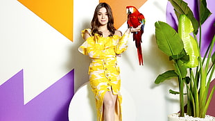 woman wearing yellow cold-shoulder button-up dress while holding a red parrot