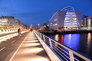 photo of people riding bike on bridge near concrete buildings during daytime, dublin