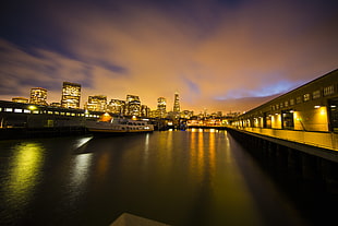 city rise buildings with seaside and bridge during nightime HD wallpaper