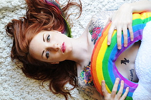 woman with tattoo laying and holding rainbow pillow