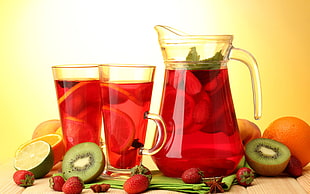red liquid filled clear glass pitcher and mug surrounded by fruits