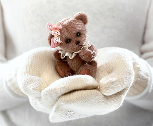 person in white gloves with brown bear plush toy