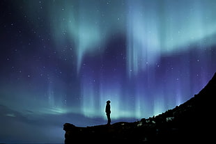 silhouette of person standing on hill cliff during nighttime