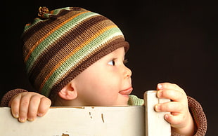 baby wearing brown, orange, and green knit hat