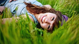 close up photography of woman in teal tank top lying in green grass field