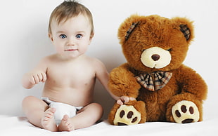 baby beside a brown teddy bear