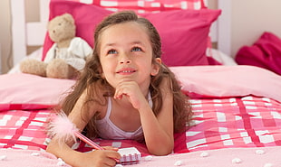 blonde haired girl wearing white top lying on pink bed